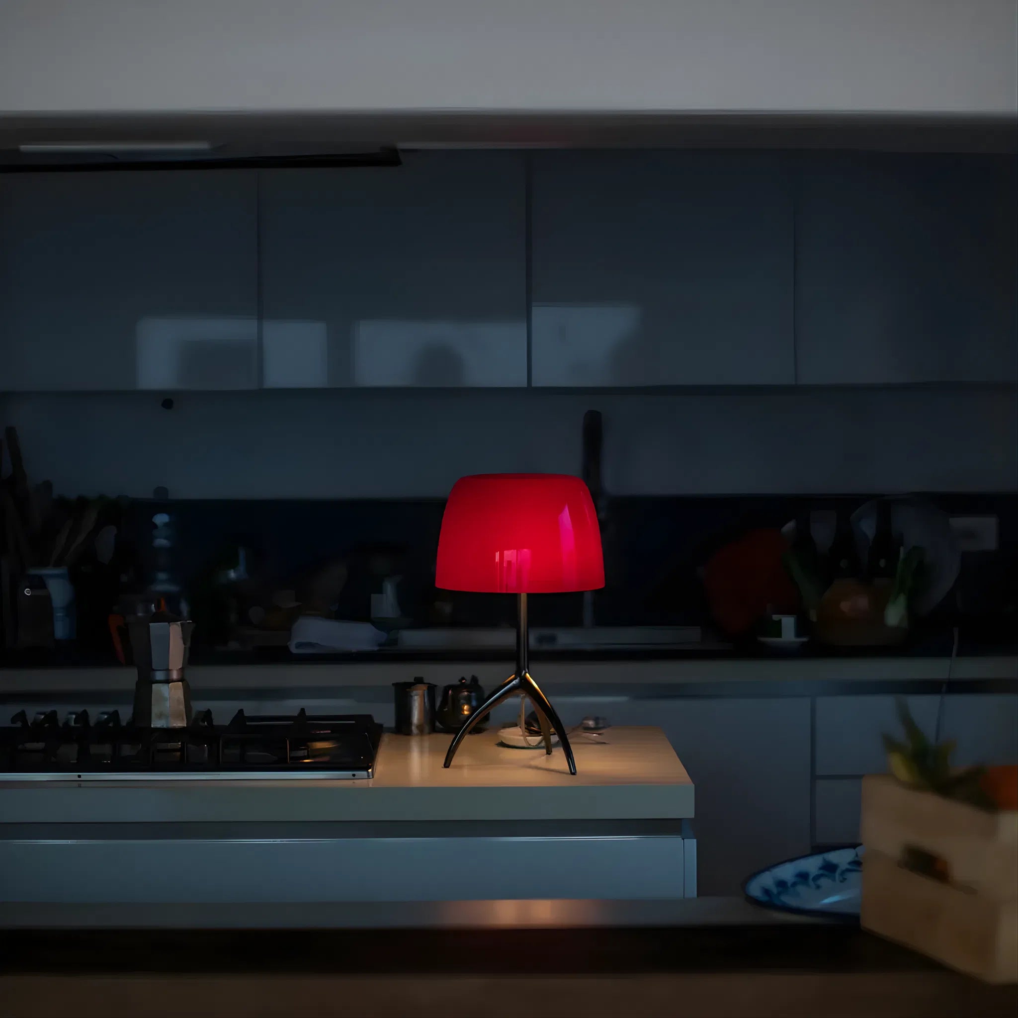 Bellaro Tri-Leg Retro Table Lamp in red casting warm ambient glow on a bedside table in a dark moody bedroom