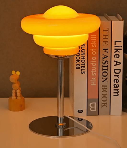 Bergamo Conch Shell Table Lamp in orange glowing on a styled shelf beside fashion books